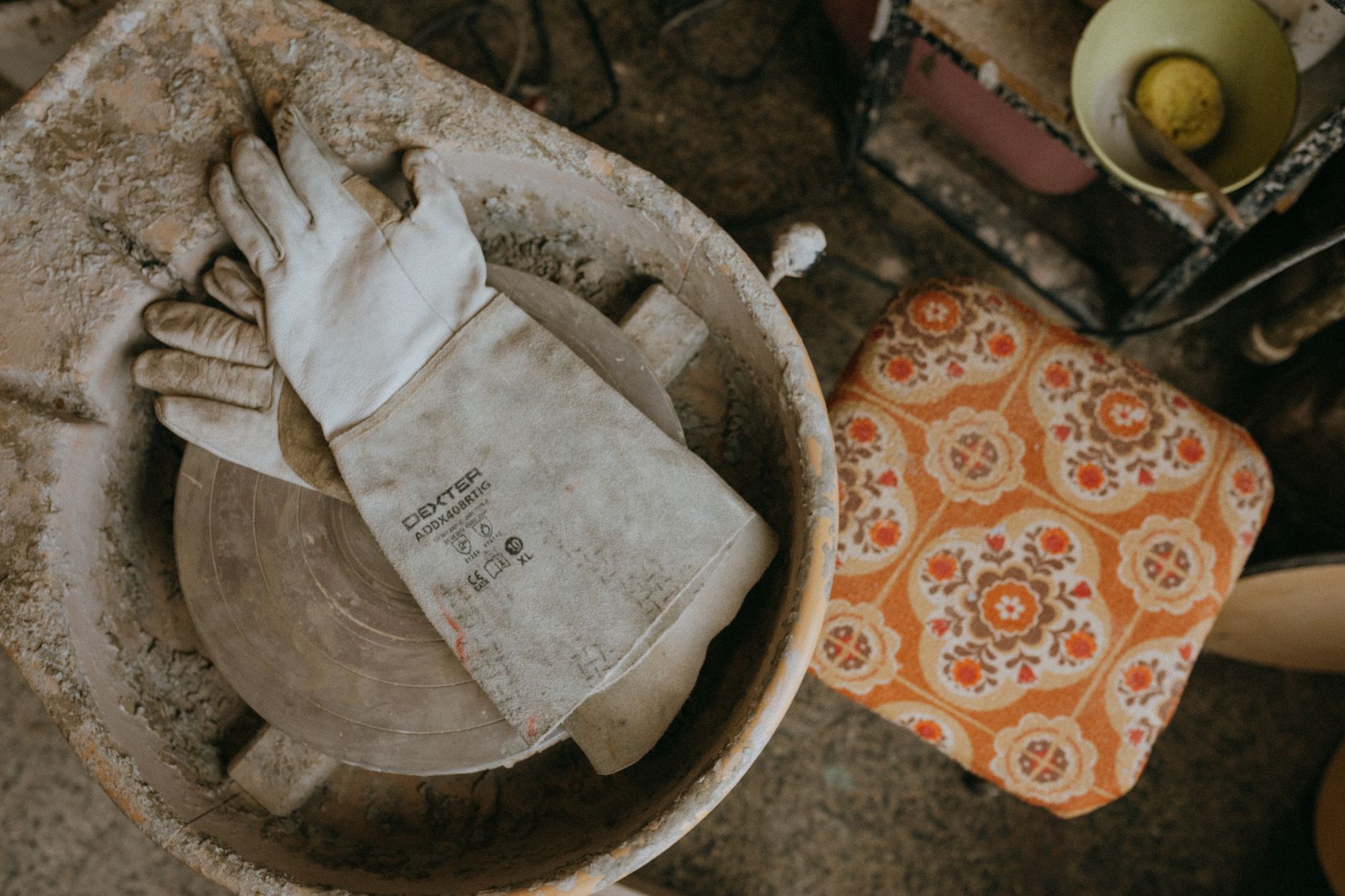 Gros plan d'un tour de potier avec des gants dans un atelier de céramique rustique.